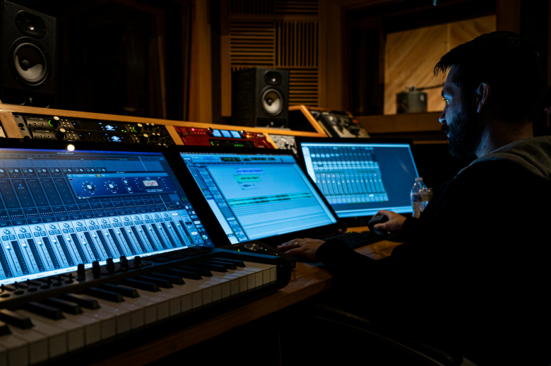 person in a music studio with multiple screens and a midi keyboard