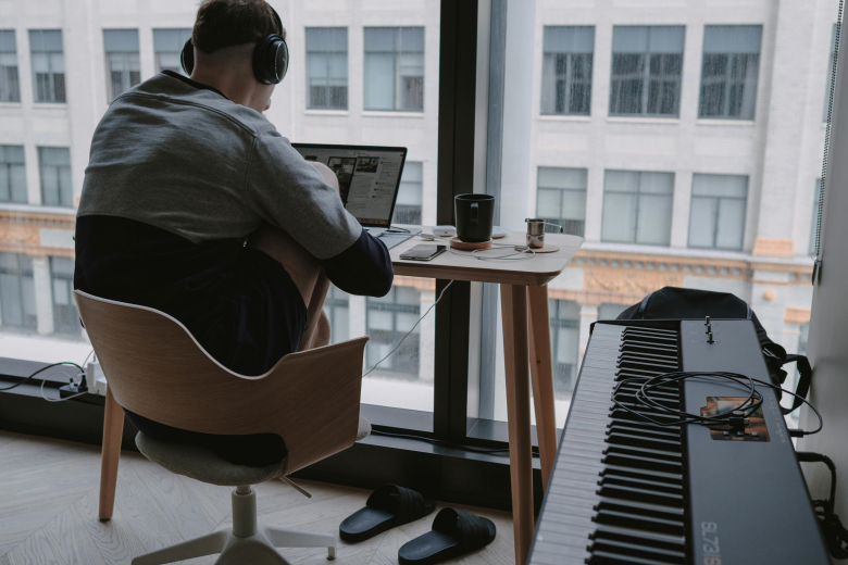 man working on computer with digital piano beside him